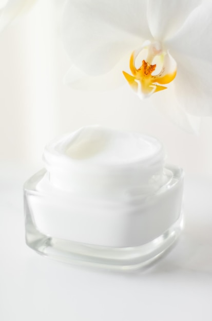 Face cream moisturizer in a jar and blooming orchid flower on white background skin care cosmetics