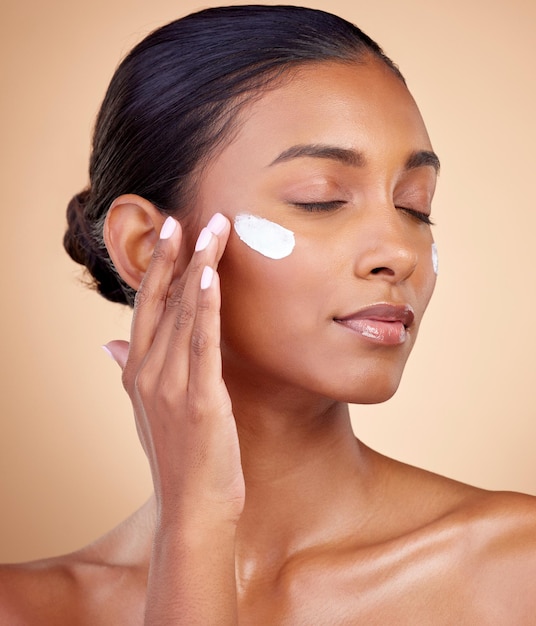 Face cream and woman with eyes closed for skincare cosmetics dermatology or aesthetic makeup on studio background Indian female model lotion and facial sunscreen for clean beauty glow and shine