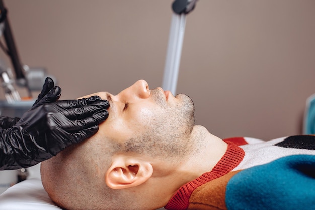 The face of a cute guy in closeup lying on a couch in a beauty salon receiving a procedure to improve the condition of the skin