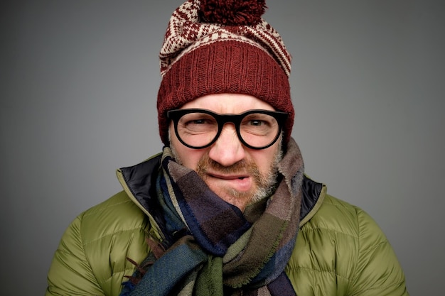 Face of european angry and furious male in warm clothes and glasses on a gray background