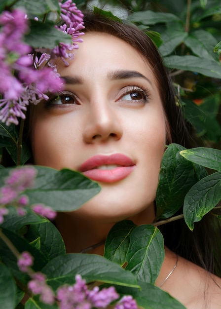 Face of a European young beautiful woman among lilac flowers and green leaves