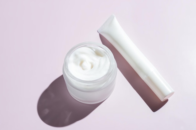 Face and eye cream in white unbranded packaging on pink background with harsh shadows Skin care daily products for healthy and fresh skin Packaging design