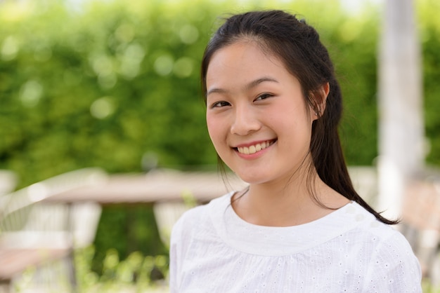 Face of happy young beautiful Asian woman smiling at the coffee shop outdoors