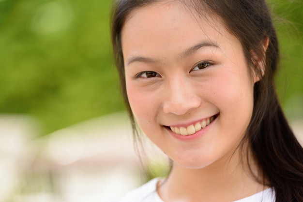 Face of happy young beautiful Asian woman smiling outdoors