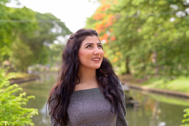 Face of happy young beautiful Indian woman thinking at the park outdoors