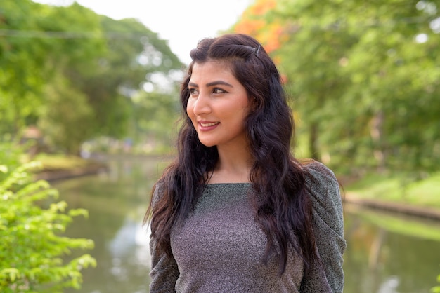 Face of happy young beautiful Indian woman thinking at the park outdoors