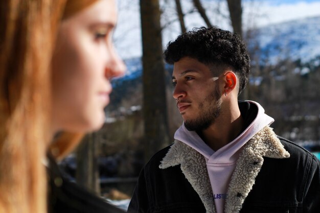 Photo face of a latin guy looking to the side with his partners face in the foreground in winter