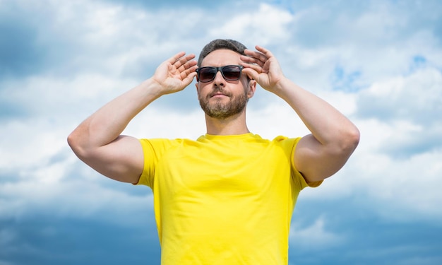 Face of man in yellow shirt and sunglasses outdoor on sky background