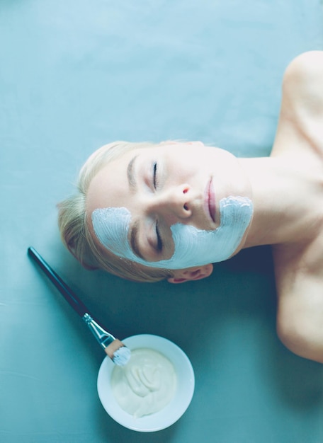 Face maskbeautiful young girl at spa cosmetician woman applying facial mask