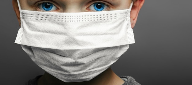 Face of a maskwearing boy with fear in the eye Closeup on a gray background