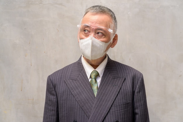 Face of mature Japanese businessman with mask and face shield thinking