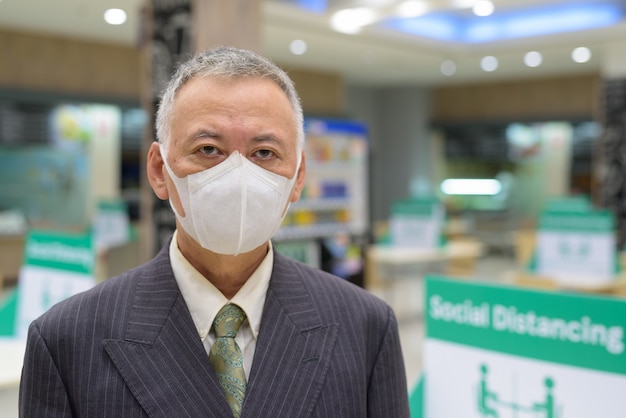 Face of mature Japanese businessman with mask social distancing at the food court