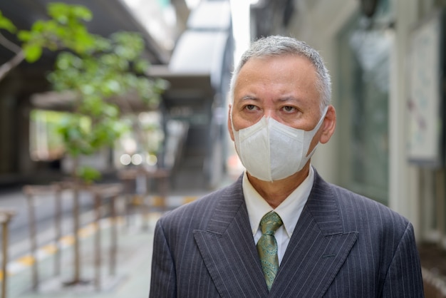 Face of mature Japanese businessman with mask thinking in the city