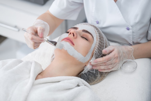 Face peeling mask, spa beauty treatment, skincare. Woman getting facial care by beautician at spa salon