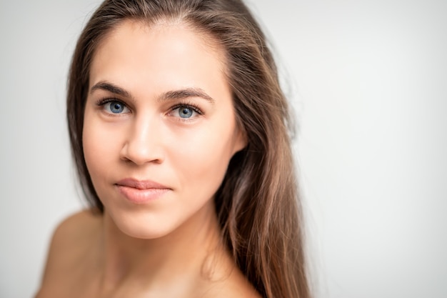 Face portrait of young caucasian woman with natural make up and eyelash extensions looking at camera on white background