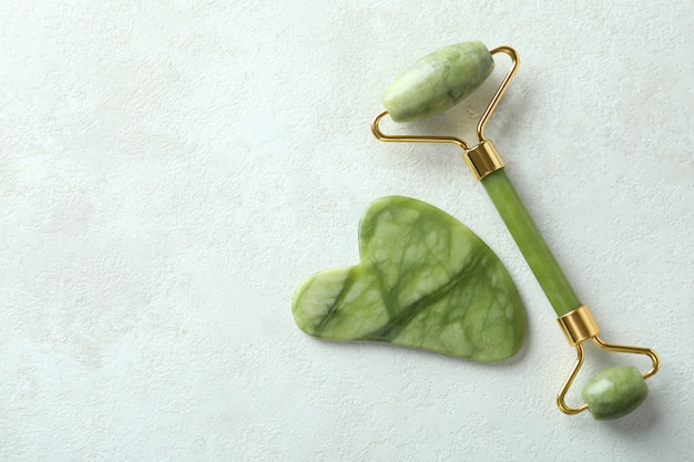 Face roller and gua sha on white textured background