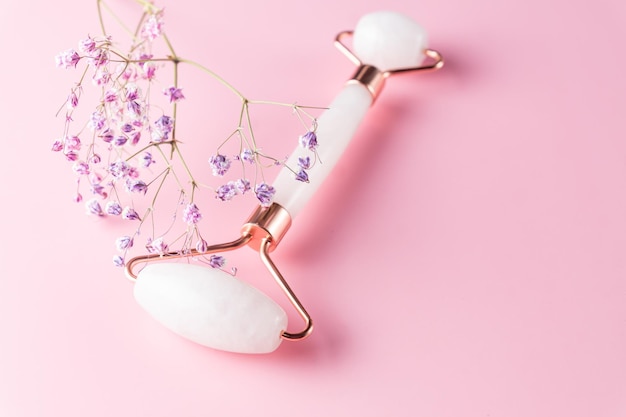 Photo face roller and gypsophila flower on pink background massage tool for facial skin care spa beauty