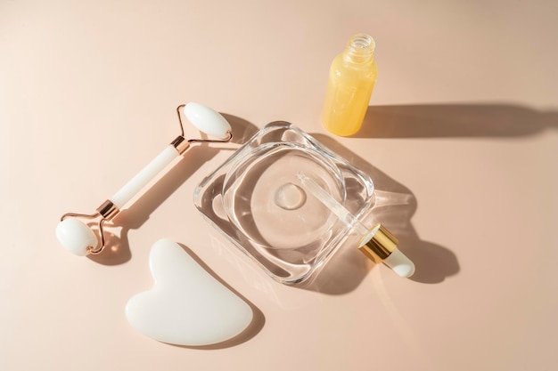 A face roller and quartz massager in the form of the heart a face brush and a face serum with vitamin C lying on the beige background