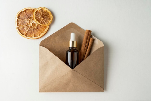 A face serum or essential oil for Christmas holidays in a brown dropper bottle lying in a brown envelope with cinnamon and dried oranges around it