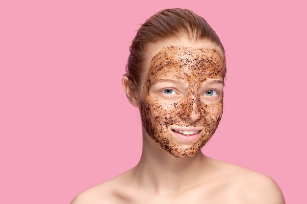 Photo face skin scrub. portrait of sexy smiling female model applying natural coffee mask, face scrub on facial skin. closeup of beautiful happy woman with face covered with beauty product.