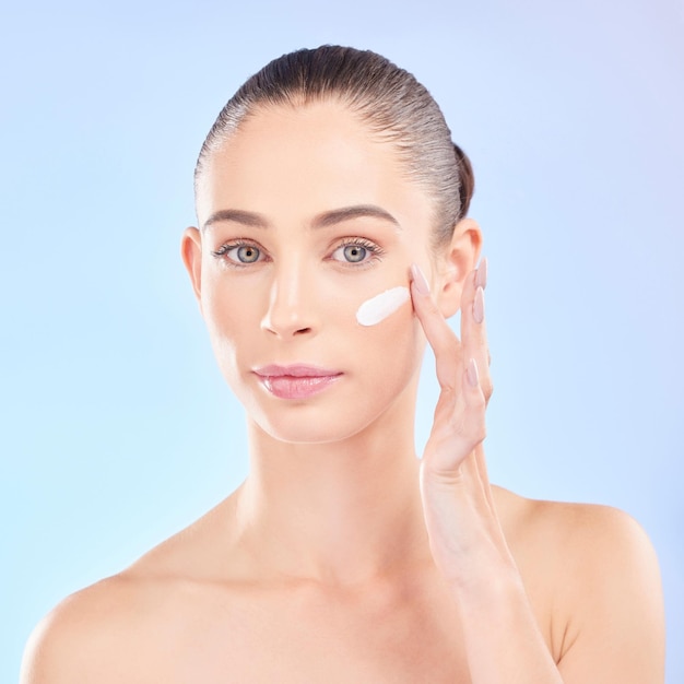 Face skincare and woman with cream in studio isolated on a blue background Portrait dermatology and serious model with creme cosmetic or sunscreen moisturizer for health aesthetic or wellness