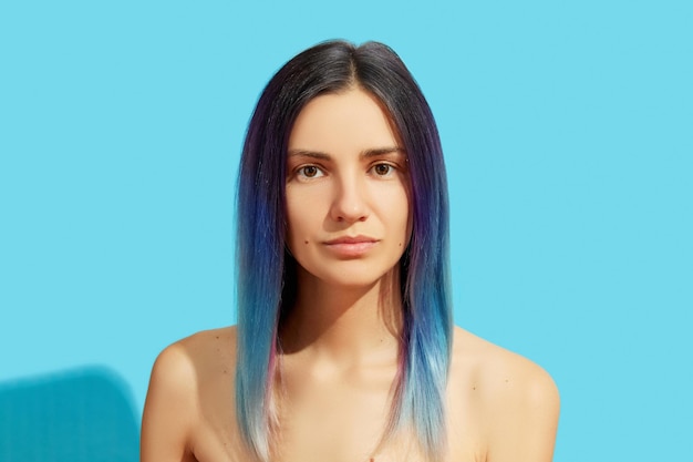 Face of young beautiful woman with blue hair on bright background Beauty salon treatment concept