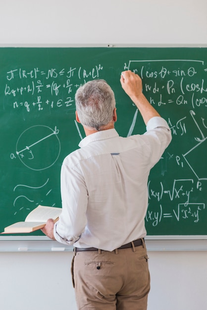 Faceless lecturer chalking formula on blackboard