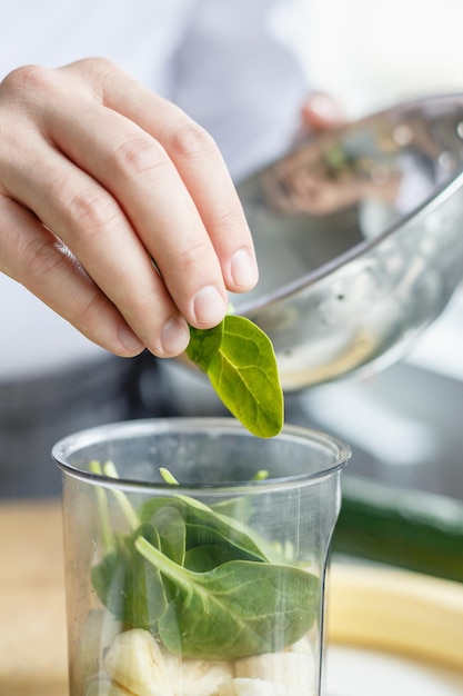 Faceless shot of male chef putting spinach leaved in content while preparing moothie