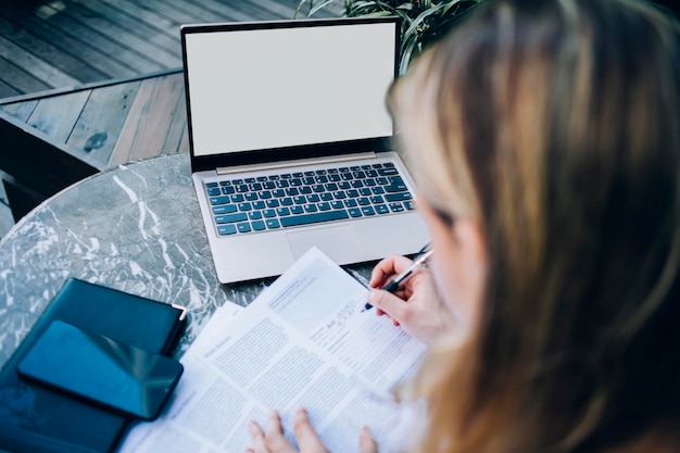 Faceless woman filling out documents during work on laptop