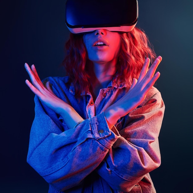 Facial expression of young girl with virtual reality glasses on head in red and blue neon in studio