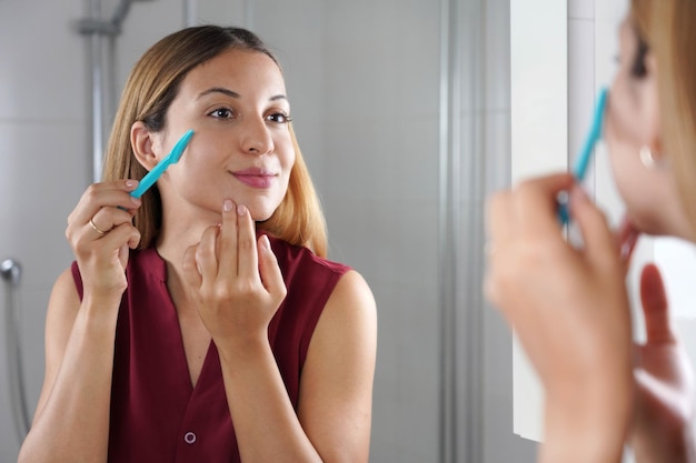 Facial hair removal Brazilian girl shaving her face by razor at home Beautiful young woman using razor on bathroom