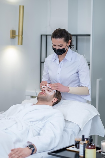 Facial mask. Female specialist applying facial mask on mans face