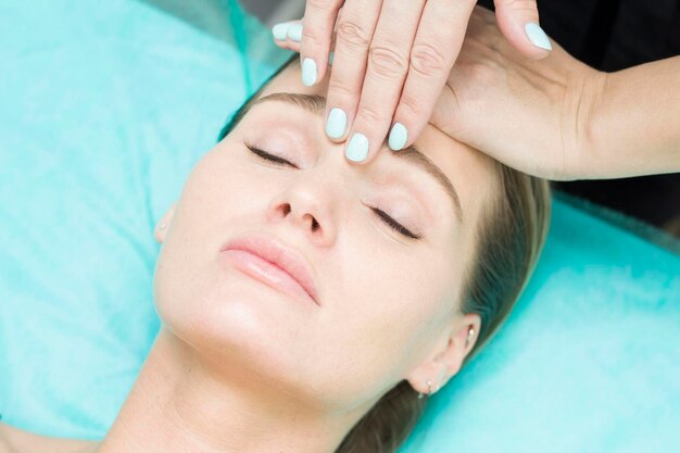 Facial massage Closeup of a young woman getting a spa massage in a spa beauty salon Facial beauty care Cosmetology Turquoise background