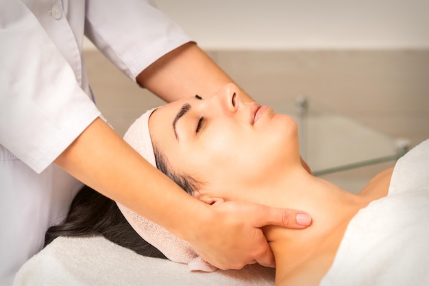 Facial massage young caucasian woman getting a massage on her neck in a beauty clinic