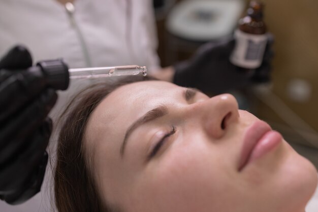 Facial skin care and protection. A young woman at a beautician's appointment. The specialist applies a cream mask to the face.