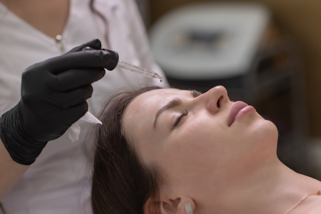 Facial skin care and protection. A young woman at a beautician's appointment. The specialist applies a cream mask to the face.