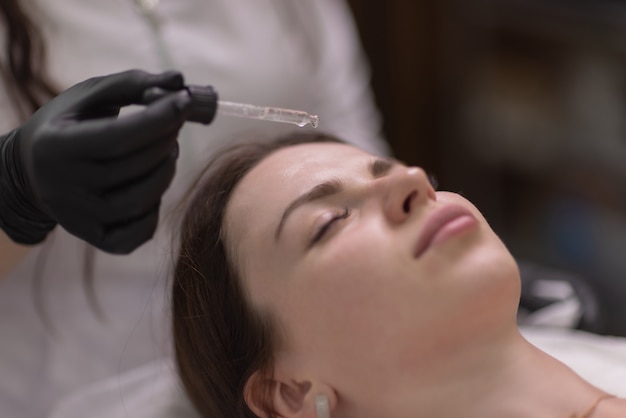 Facial skin care and protection. A young woman at a beautician's appointment. The specialist applies a cream mask to the face.