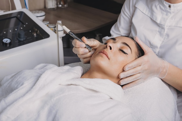 Facial skin lifting procedures on a brunette lady lying in a spa salon healed with new apparatus