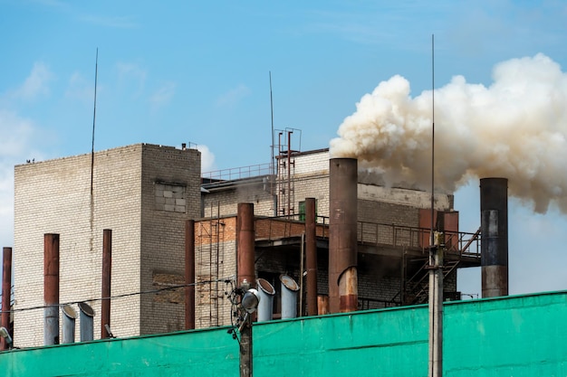 Factory chimneys against the gray autumn sky Utopian landscape background White toxic smoke is coming from a huge pipe Pollution of the environment and nature The collapse of civilization