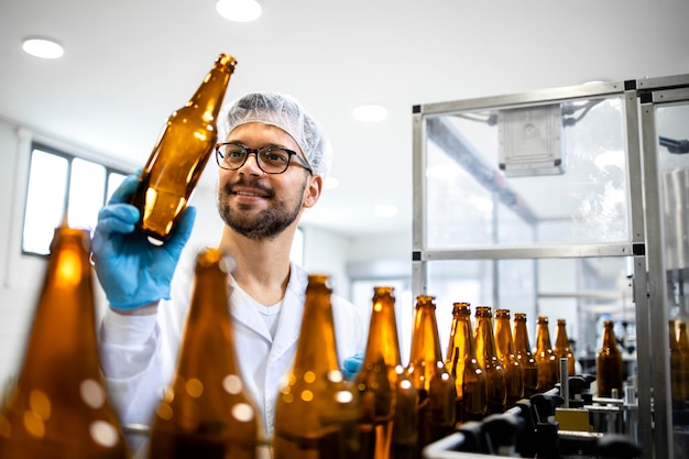 Factory technologist checking glass bottle purity and cleanliness in beer beverage bottling plant