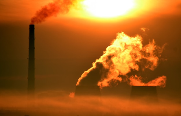 Factory with chimneys and Smoke in the Orange Glare of the Dawn and Morning Fog in the Summer. Bright Sun Shines Through Smoke Plant, Power Plant. Industrial Background