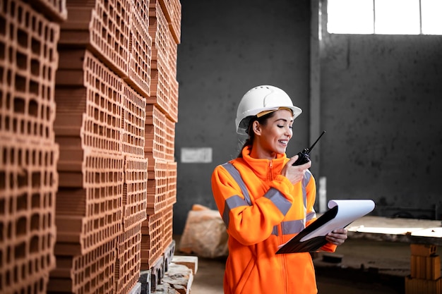 factory worker standing by the pile of clay bricks for construction industry and checking inventory