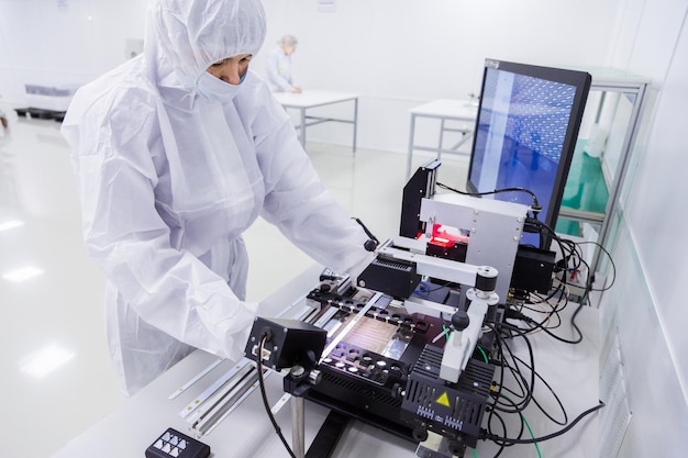 A factory worker in a white lab suit latex gloves and face mask working with some modern equipment during the manufacturing of a tv set