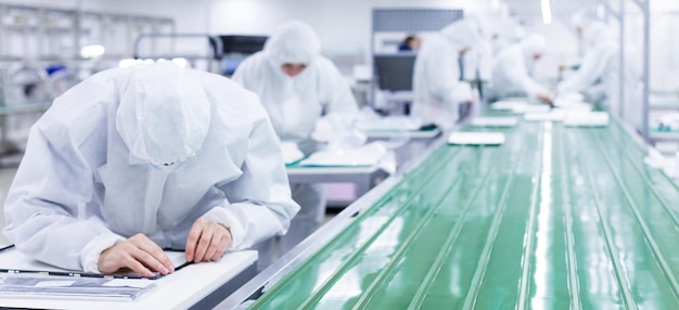 Factory workers in white lab suits and face masks producing tv sets on a green assembly line blurred background