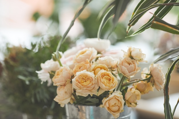 Faded background image of beautiful pale roses arranged in flower composition at green florists workshop, copy space