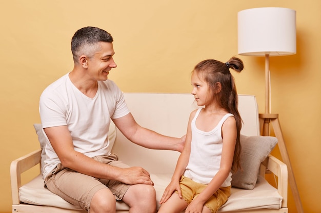 Faily relationship Happy parenthood father with child daughter wearing casual clothing sitting on sofa against beige background pleasant conversation