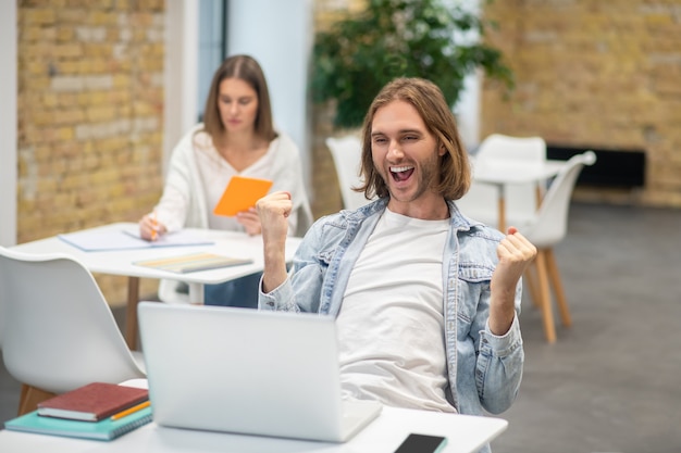 Fair-haired young man sitting at the laptop and looking excited