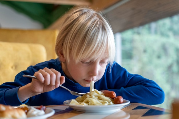 Fairhaired teenager at table eating pasta Child boy is having lunch Student eating in the school cafeteria