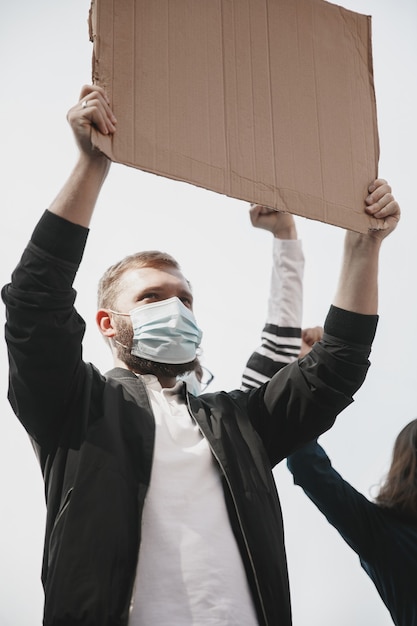 Faith. Group of activists giving slogans in a rally. Caucasian man and woman marching together in a protest in the city. Look angry, hopeful, confident. Blank banners for your design or ad.