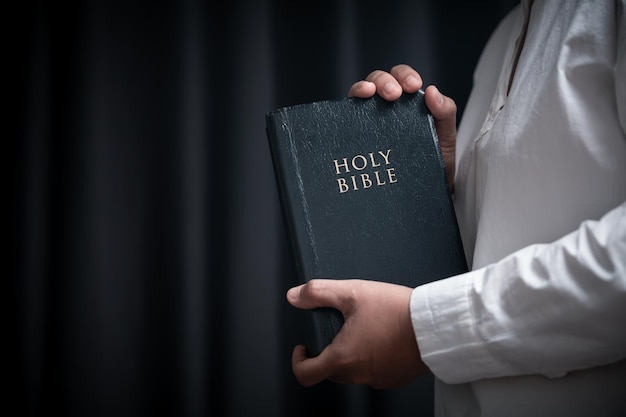 Faith with holy bible concept Hands of a female prayer worship God with holy bible on black background in church Christian woman who believe in Jesus read and study the grace of the holy scriptures